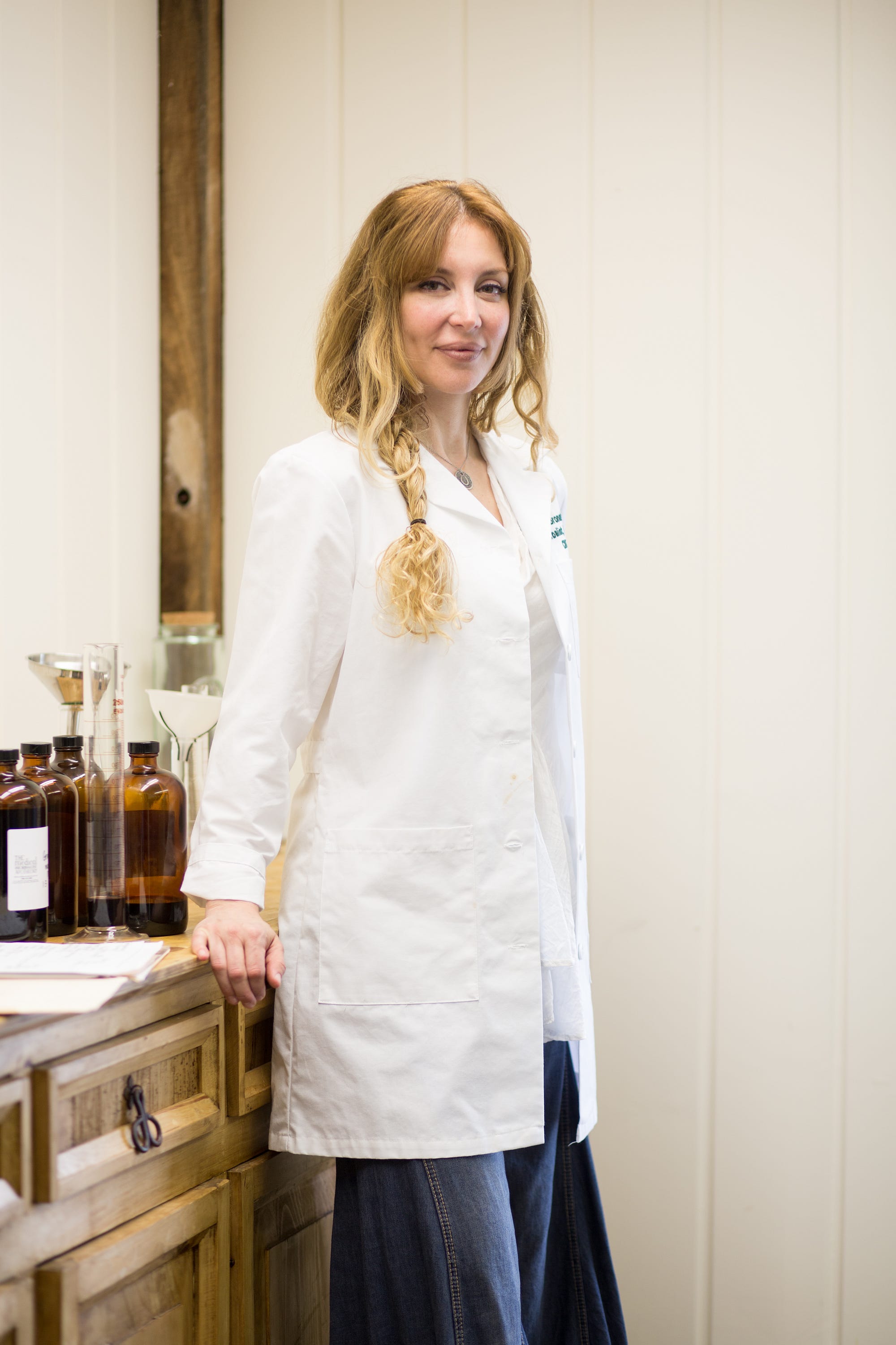 Tami poses in a white coat with herbal products behind her