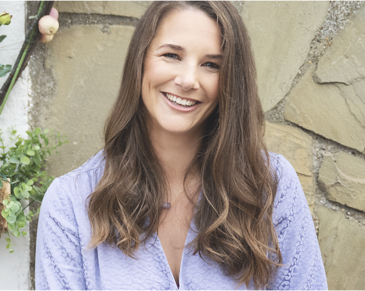 Marjolein smiling in purple top against a wall.